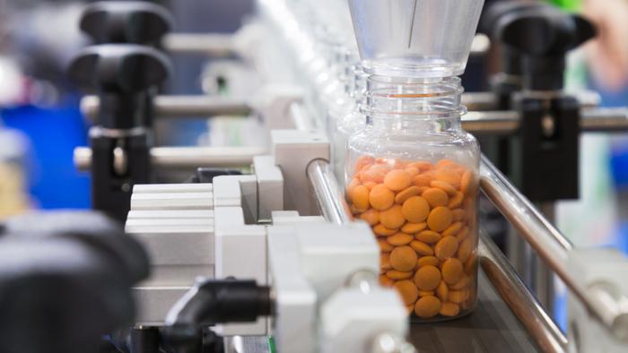 Pill bottles are mechanically filled with orange tablets at a digital pharmacy's central fill center. 